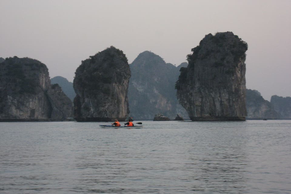 Two kayakers crossing calm water between Lan Ha Bay's limestone islands