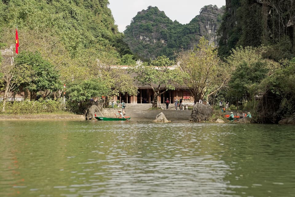 Rowboats passing a riverside temple below Ninh Binh's limestone cliffs